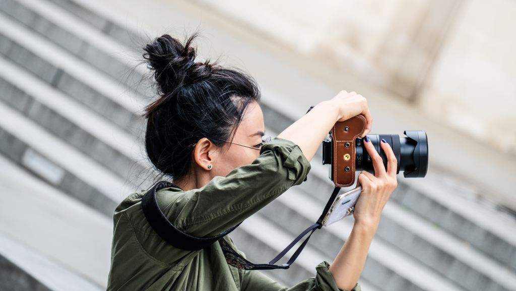 Woman holding black DSLR camera and taking picture at daytime
